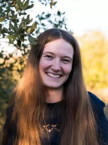 Aili Channer smiling to camera, standing in front of some green foliage