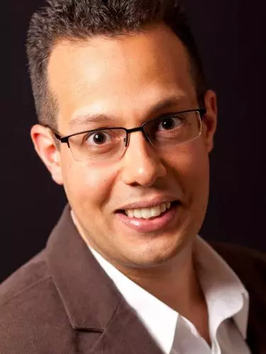 Photo of John-Paul Ghobrial smiling to camera in front of a black background.