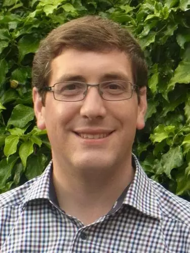 Photo of Christian Leitmeir smiling to camera, standing outside in front of foliage. 