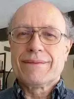 Photo of David Norbrook smiling to camera with a bookshelf behind him.