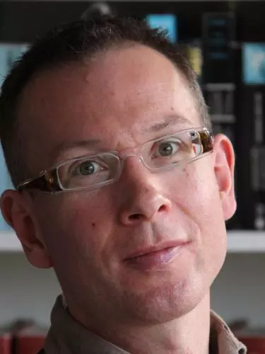 Photo of Bart Van Es looking to camera with a bookshelf behind him
