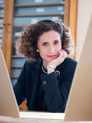 Photo of Geraldine Johnson looking to camera with her hand on her cheek, sitting in front of a cabinet. 