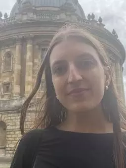 Head and shoulder shot of a woman wearing a black shirt standing in front of the Radcliffe Camera.