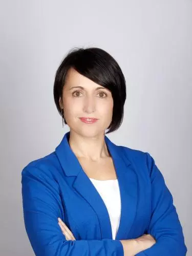 Photo of Diana Berruezo Sanchez looking to camera with her arms folded, standing in front of a white background.