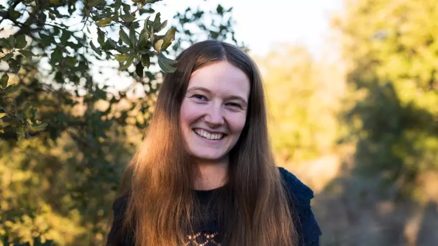 Aili Channer smiling to camera, standing in front of some green foliage