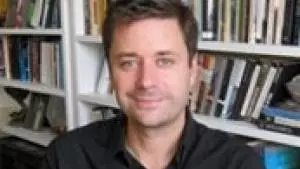 Photo of Adam Smyth smiling to camera with a bookcase behind him