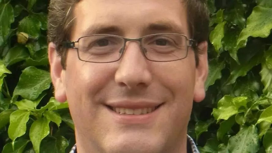 Photo of Christian Leitmeir smiling to camera, standing outside in front of foliage. 