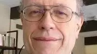 Photo of David Norbrook smiling to camera with a bookshelf behind him.