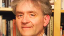 Photo of Richard Lawes looking to camera with a bookcase behind him.
