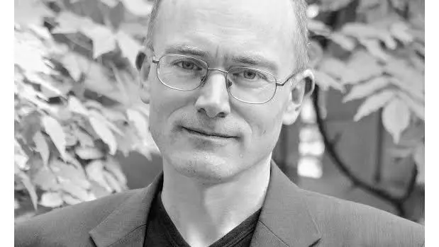 Black and white photo of Peter Wilson standing outside in front of foliage.