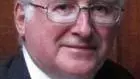 Photo of Ian Maclean looking to camera in front of a wooden panel.