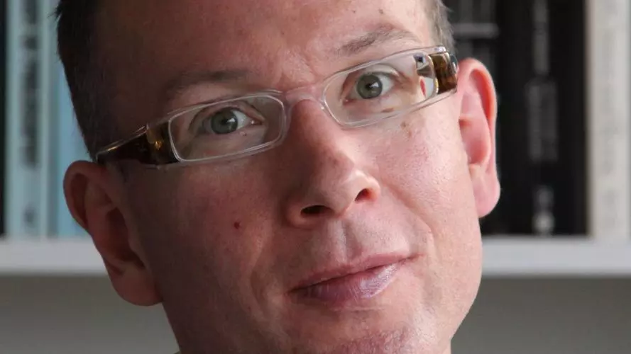 Photo of Bart Van Es looking to camera with a bookshelf behind him