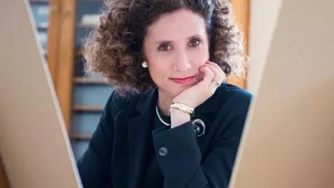 Photo of Geraldine Johnson looking to camera with her hand on her cheek, sitting in front of a cabinet. 
