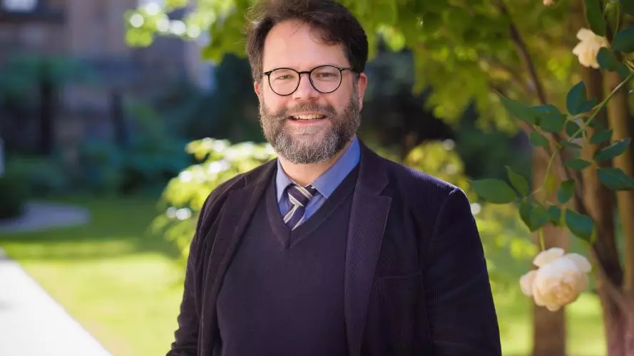 Photo of Dr Christoph Schmitt-Maass wearing a dark suit with blue and yellow tie. Bearded and wearing glasses, smiling at camera.